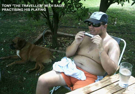 Tony sitting outside at a table playing the harmonica