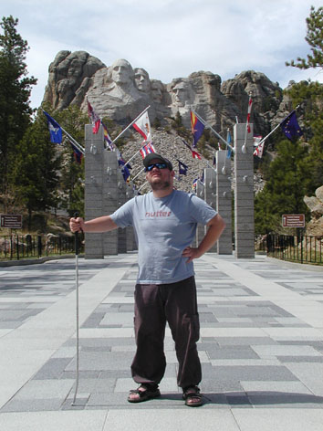 Tony standing in front of granite pillars flying the 56 flags. Mount Rushmore in the background.