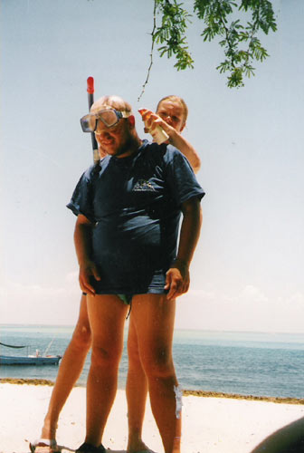 Becky spraying suntan lotion on Tony